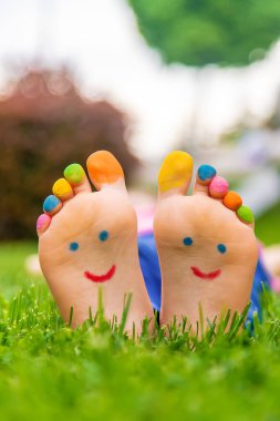 Çimlerin üzerinde boyalı bir gülümsemeyle bir çocuğun ayakları. Seçime odaklan. Çocuk.