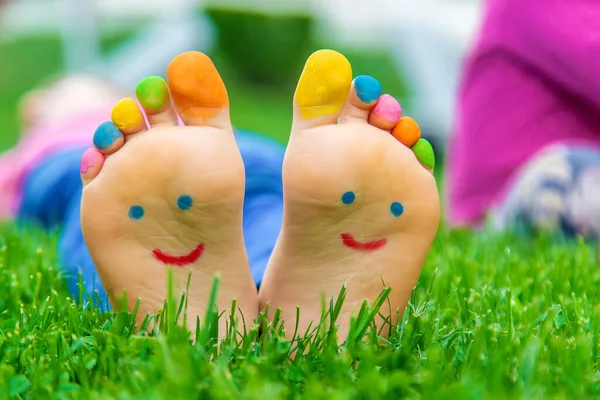 Çimlerin üzerinde boyalı bir gülümsemeyle bir çocuğun ayakları. Seçime odaklan. Çocuk.