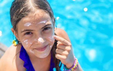 Havuzun yanındaki çocuk güneş kremi sürüyor. Seçime odaklan. Çocuk.