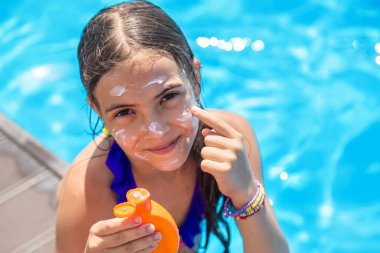 Havuzun yanındaki çocuk güneş kremi sürüyor. Seçime odaklan. Çocuk.