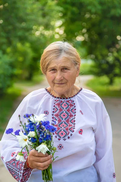 An old Ukrainian woman in an embroidered shirt with a bouquet of flowers. Selective focus. Nature.