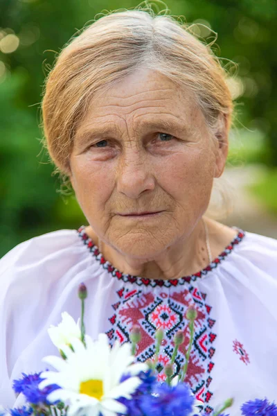 An old Ukrainian woman in an embroidered shirt with a bouquet of flowers. Selective focus. Nature.