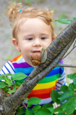 The child looks at the snail. Selective focus. Nature.