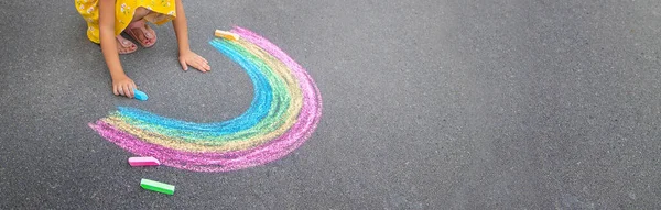 A child draws a rainbow on the asphalt. Selective focus. kid.