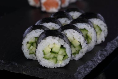 Salatalık ve pirinçle yuvarlan. Suşi ve siyah arka planda rulo