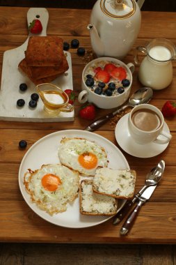 Çırpılmış yumurtalı kahvaltı, meyveli müsli, kahverengi ahşap arka planda sütlü kahve.
