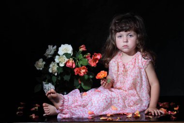 Bir buket gülün yanında oturan küçük bir kız