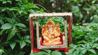 Lord Ganesha idol sitting in decorated swing in Ganesh Chaturthi festival in India. The Elephant god statue with nature background. Also known Vinayaka Chaturthi, Pillaiyar