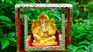Lord Ganesha idol sitting in decorated swing in Ganesh Chaturthi festival in India. The Elephant god statue with nature background. Also known Vinayaka Chaturthi, Pillaiyar