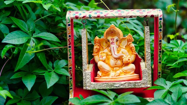 Lord Ganesha idol sitting in decorated swing in Ganesh Chaturthi festival in India. The Elephant god statue with nature background. Also known Vinayaka Chaturthi, Pillaiyar