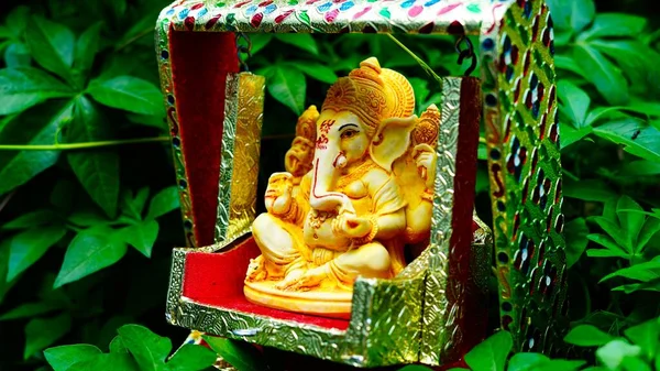 Lord Ganesha idol sitting in decorated swing in Ganesh Chaturthi festival in India. The Elephant god statue with nature background. Also known Vinayaka Chaturthi, Pillaiyar