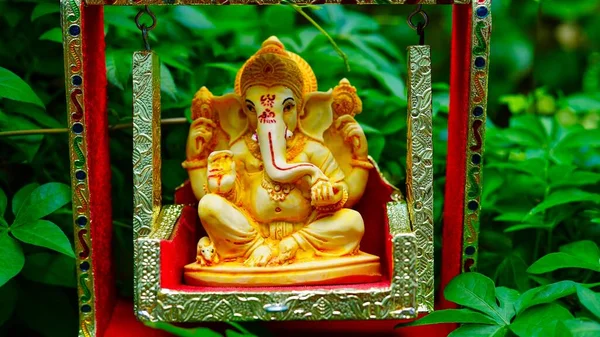 Lord Ganesha idol sitting in decorated swing in Ganesh Chaturthi festival in India. The Elephant god statue with nature background. Also known Vinayaka Chaturthi, Pillaiyar
