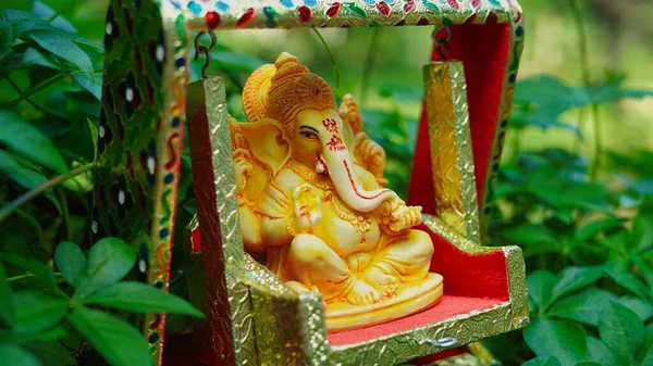 Lord Ganesha idol sitting in decorated swing in Ganesh Chaturthi festival in India. The Elephant god statue with nature background. Also known Vinayaka Chaturthi, Pillaiyar