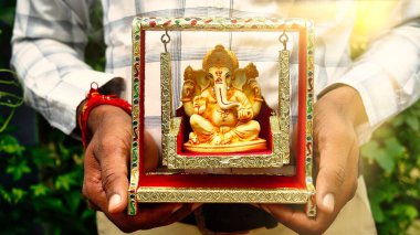 A Man holding Ganesha idol for Visarjan or Immersion in water annual ritual during Ganesh Chaturthi Hindu festival. Lord Ganapati idol in hands with sun rays background. Ganesh utsav in India