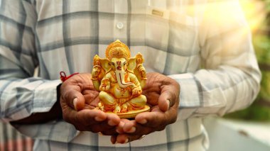 A Man holding Ganesha idol for Visarjan or Immersion in water annual ritual during Ganesh Chaturthi Hindu festival. Lord Ganapati idol in hands with sun rays background. Ganesh utsav in India