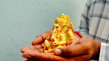 A Man holding Ganesha idol for Visarjan or Immersion in water annual ritual during Ganesh Chaturthi Hindu festival. Lord Ganapati idol in hands with sun rays background. Ganesh utsav in India
