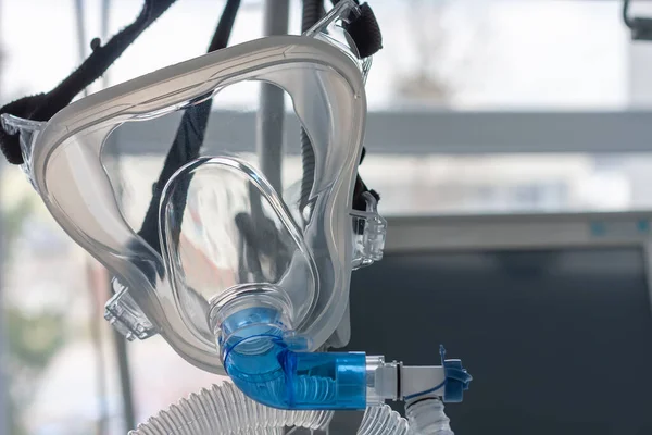 Non-invasive ventilation face mask, close up view, on background medical ventilator in ICU in hospital.