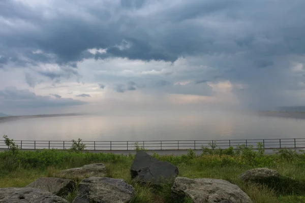 Upper water reservoir of the pumped storage hydro power plant Dlouhe Strane in Jeseniky Mountains, Czech Republic. During summer foggy rainy morning, sunrise, storm clouds.