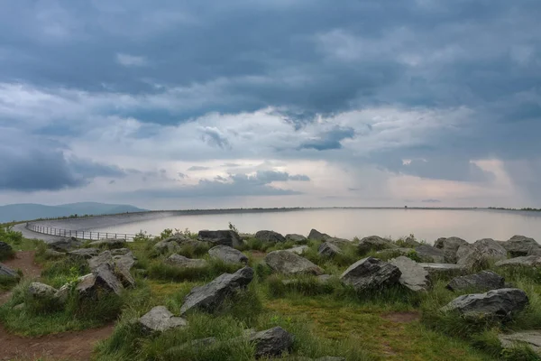 Upper water reservoir of the pumped storage hydro power plant Dlouhe Strane in Jeseniky Mountains, Czech Republic. During summer rainy morning, sunrise, storm clouds.