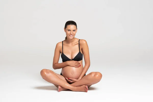 Junge schöne schwangere Frau auf dem Boden, die Unterwäsche anzieht. horizontal — Stockfoto