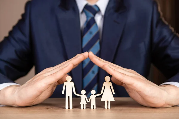 Takım elbiseli ve kravatlı bir adam aile üzerinde bir ev şeklinde el ele tutuşuyor. Sigorta konsepti.