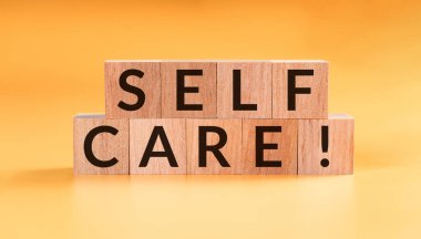SELF CARE - text building from wooden cubes on yellow background.