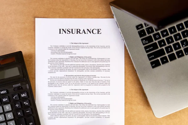 Flat lay of insurance policy with laptop and calculator on the wooden table.