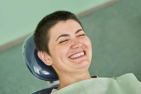 Diş hekimliğinde gülümseyen kadın hasta portresi. Genç bir kadın dişçi koltuğunda oturup gülüyor..