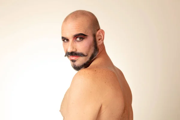 Portrait of bald man without shirt and makeup looks at camera with bare back.  Image in low angle. Side view of caucasian drag man with beard.