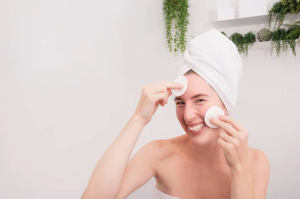 Skin cleansing. Portrait of woman cleaning her face using soft cotton. She is looking at camera playfully. Beauty concept and isolated background