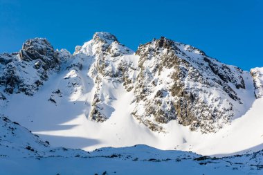Sabah güneşinde dağın tepelerindeki karlı vadiden manzara. Çiğ dağ manzarası, dağcıları ve sıra dışı kayak ve snowboard hayranlarını cezbediyor..