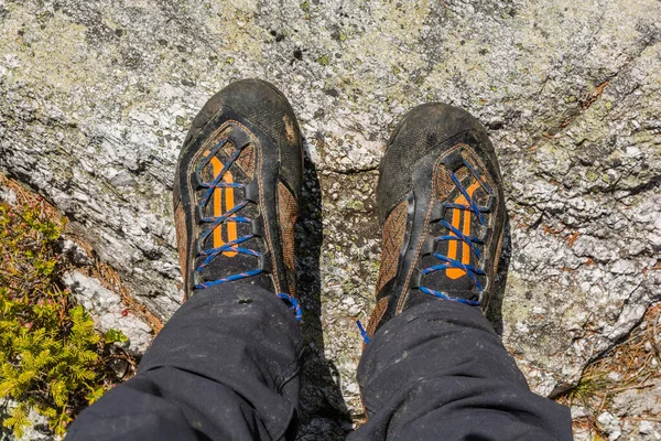 Mountain boots on a tourist\'s feet do not have an easy life. A tourist standing on a rock in dirty shoes and pants after the hardship of the trip.