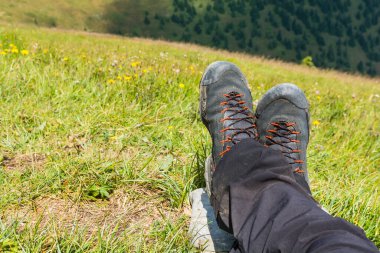 Wet approach shoes and pants drying on the legs of a tourist resting on the green grass.