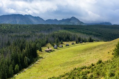 Güneş, patikanın işaretlendiği barakalarla açıklığı aydınlatıyor. Dağların üzerine yağan kara bulutlar..