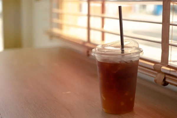 iced coffee in plastic cup Placed by the window, wooden blinds, There was an orange sunlight coming in
