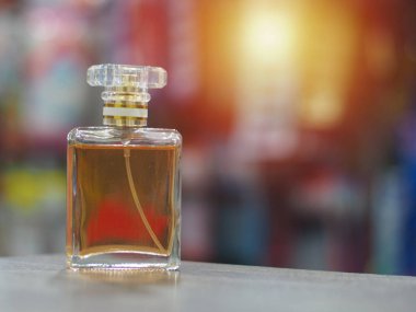 Kahverengi parfüm, berrak, kare bir şişede, arkası oldukça bulanık ve çok güzel turuncu bir parıltısı var.