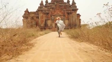 Beyaz Elbiseli Genç Turist Kadın Eski Burma Tapınağına koşuyor. Seyahat Macerası Yaşam Tarzı Tatil Konsepti. 4K Slowmotion Steadycam Beni Takip Et Görüntüsü. Bagan, Myanmar..