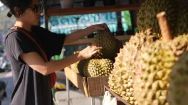 Genç turist kadın meyve pazarından taze Durian 'ı seçiyor. Yüksek kalite 4K video. Phuket, Tayland.