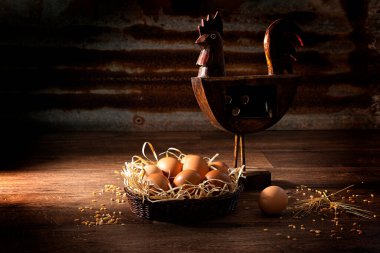 Kırsal ahşap horozla yan camdan yanan tavuk yumurtası sepeti ve kıvrımlı demir bir arka planda dağınık buğday..