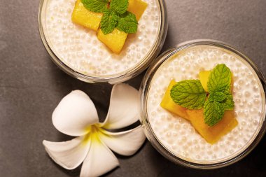 Tropical tapioca and coconut cream with mango dessert on a textured grey background  with a frangipani flower flat lay top down view.