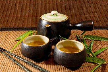 Japon çaydanlığı ve fincanları bambu hasırı üzerinde yeşil çay ile bambu yaprakları ve yemek çubuklarıyla.