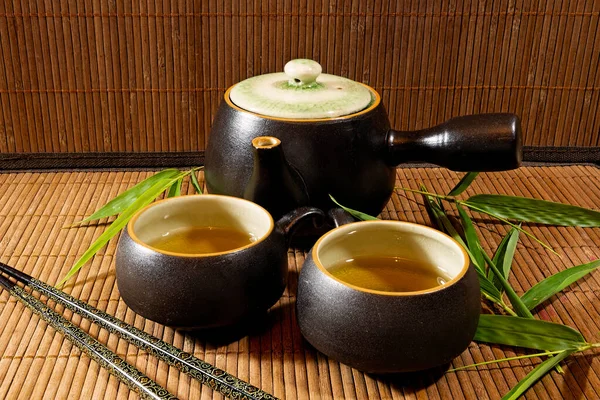 Japon çaydanlığı ve fincanları bambu hasırı üzerinde yeşil çay ile bambu yaprakları ve yemek çubuklarıyla.