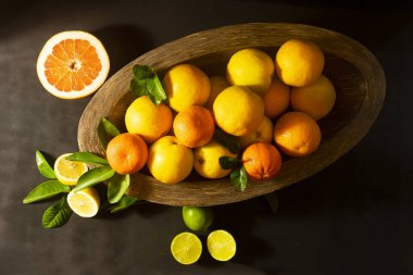 Tahta bir kase narenciye, portakal ve mandalina, dokulu siyah arka plan üzerinde düz bir görünüm aşağı yaktı.