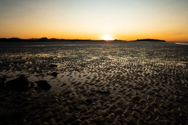 Kumda dalgalanmalar ve tropik Kuzey Queensland 'deki ışığı yansıtan küçük su birikintileriyle bir kumsalın üzerinde batan güneş..