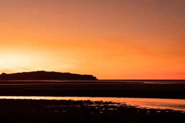 Mackay, Queensland, Avustralya 'da arka planda adaları olan tropikal bir plajda altın kırmızısı gün batımı.