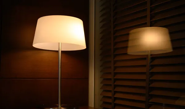 lamp or lantern glowing on wooden table next to bed with reflection glass