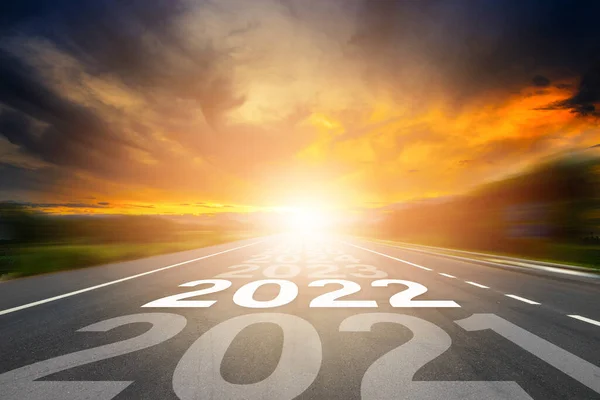 Start to New year 2022 concept. Number of the year written on highway road in the middle of empty asphalt road with sunset or sunrise light above asphalt road