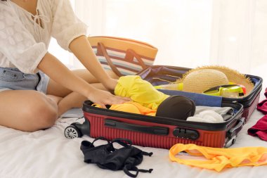 Kadın eli, yaz kıyafetlerini ve plaj aksesuarlarını yataktaki bavullara dolduruyor. Yolculuk için yeni eşyalar hazırlanıyor. Yaz tatili, tatil konsepti