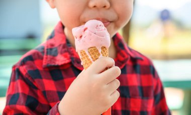 Asyalı çocuğun elinde tatlı çilekli dondurma, mutlu çocukluk konsepti, 6 yaşındaki çocuk dondurmasının tadını çıkarsın.