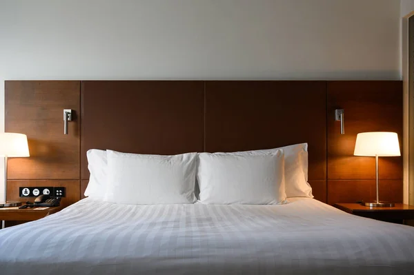 リラクゼーションのためのモダンなベッドルームスタイルでナイトスタンドに輝くランプやランタンの近くのホテルのダブルベッドのフロントビュー インテリアデザインのコンセプト — ストック写真
